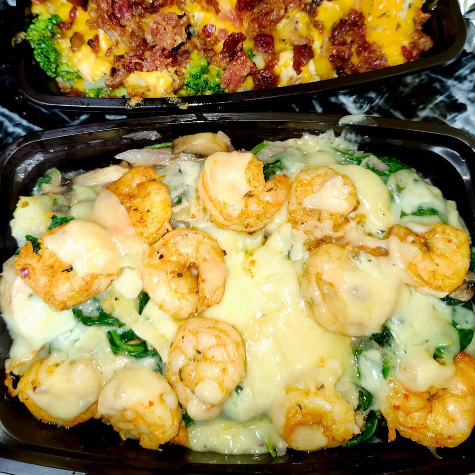 Cheesy shrimp and spinach dish in a black container, with a broccoli and bacon dish in the background.