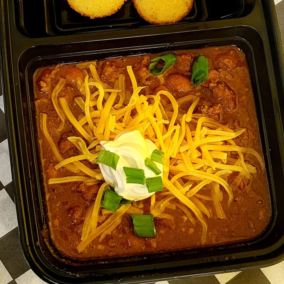 Hearty chili topped with shredded cheddar, sour cream, and green onions, served with cornbread.