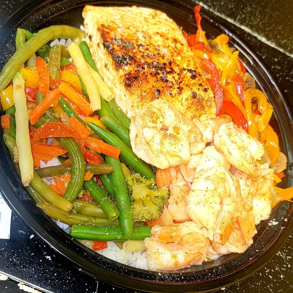 Grilled salmon and shrimp with green beans, carrots, and bell peppers in a black bowl.
