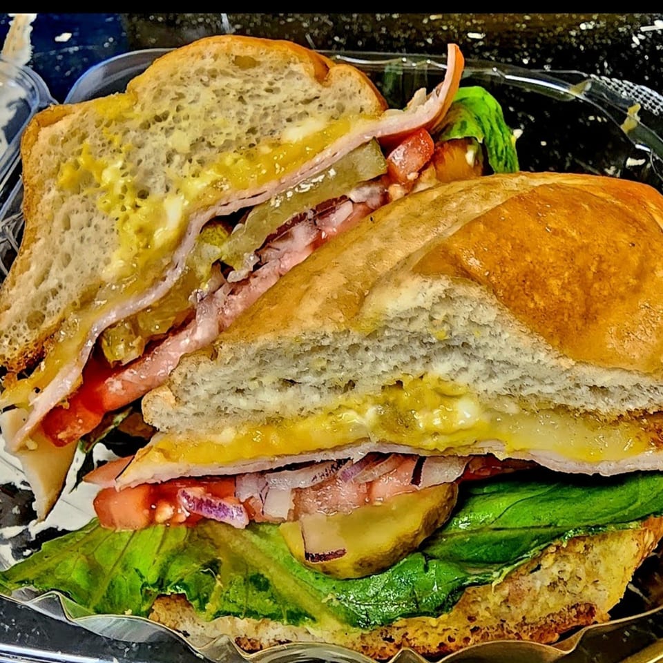 A healthy TATERSALADZ sandwich with ham, cheese, lettuce, tomatoes, and pickles in a plastic container.